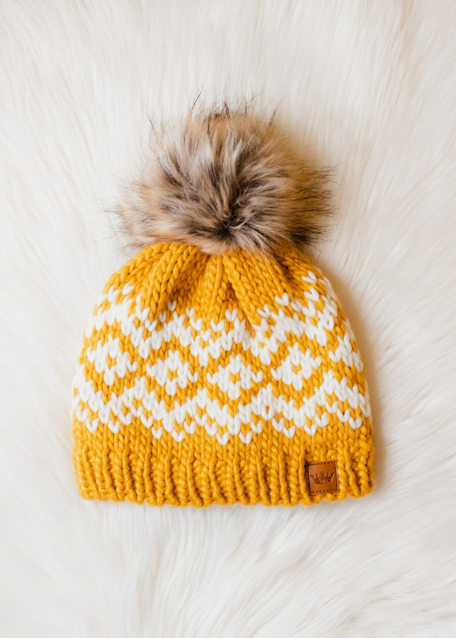 Yellow and white patterned knit hat with a fur pom-pom on a light background