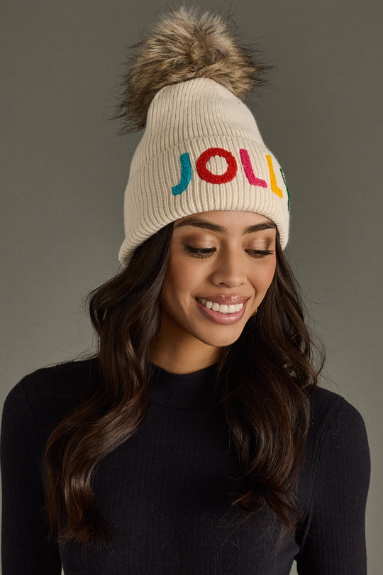 Woman wearing a beige knit beanie with colorful letters on a gray background
