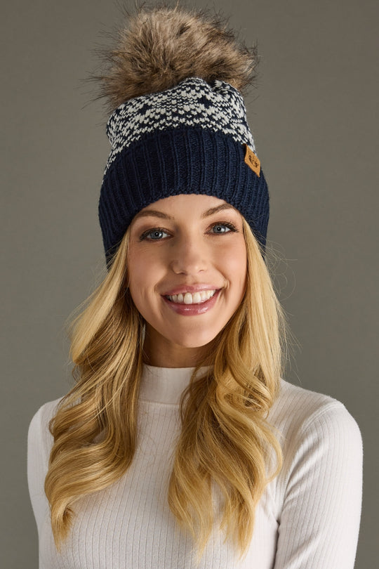 Woman wearing a navy blue knit beanie with a fur pom-pom on a gray background