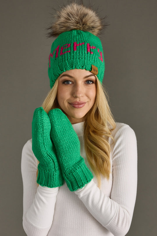 Woman wearing a green knit beanie with a fur pom-pom and matching green mittens against a gray background