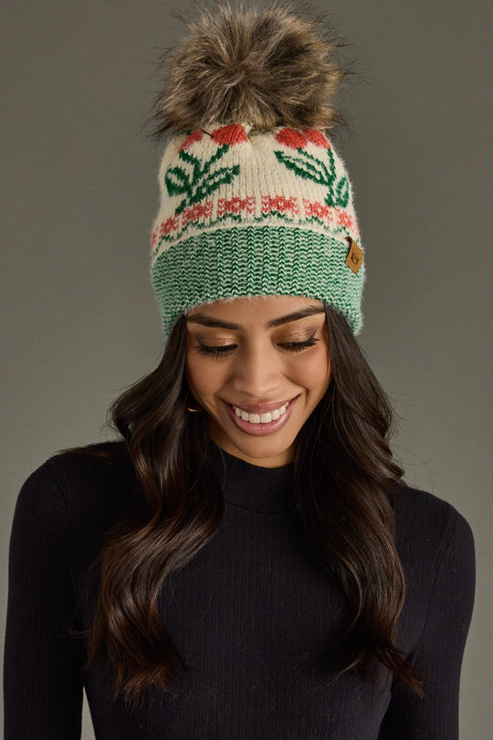 Woman wearing a green knit beanie with a pom-pom on a gray background