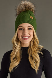 Woman wearing a green knit beanie with a fur pom-pom against a gray background