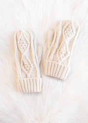 Pair of cream-colored knitted mittens on a white fur surface