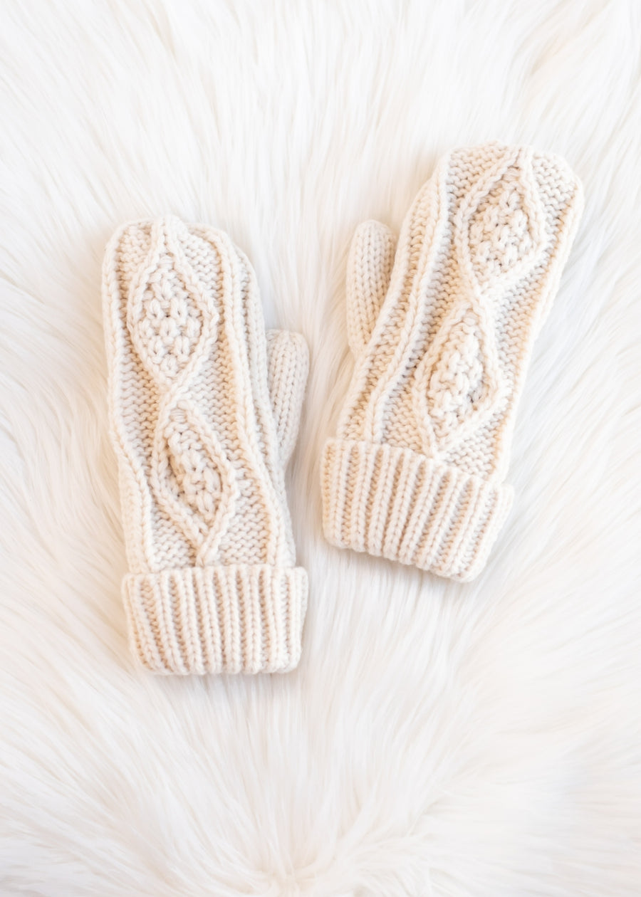 Pair of cream-colored knitted mittens on a white fur surface