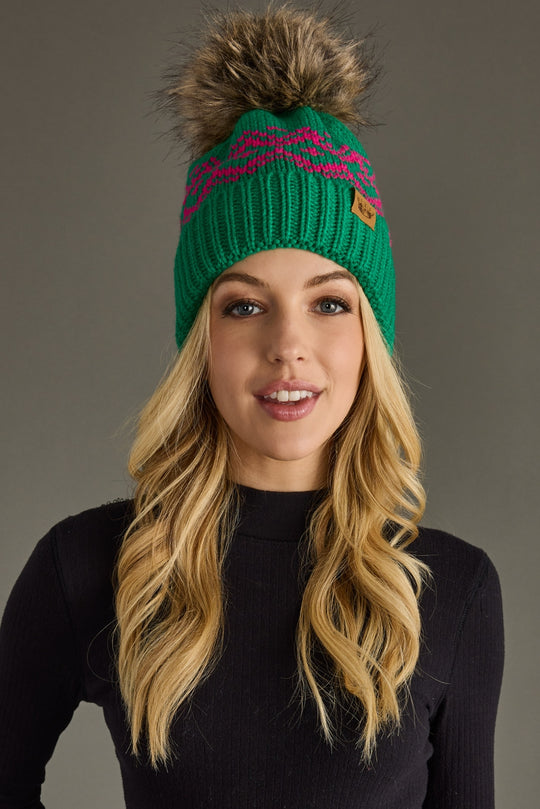 Woman wearing a green knit beanie with a pom-pom against a gray background