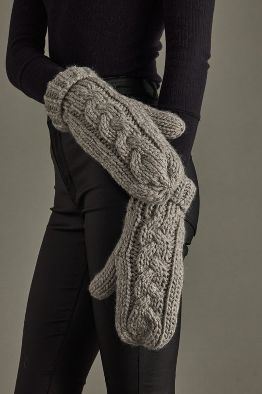 Person wearing gray knit mittens against a neutral background