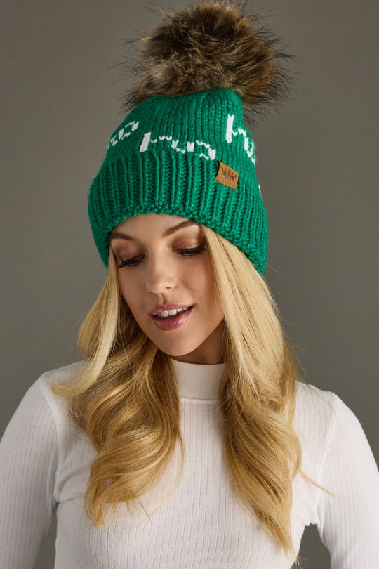 Woman wearing a green knit beanie with a fur pom-pom on a gray background
