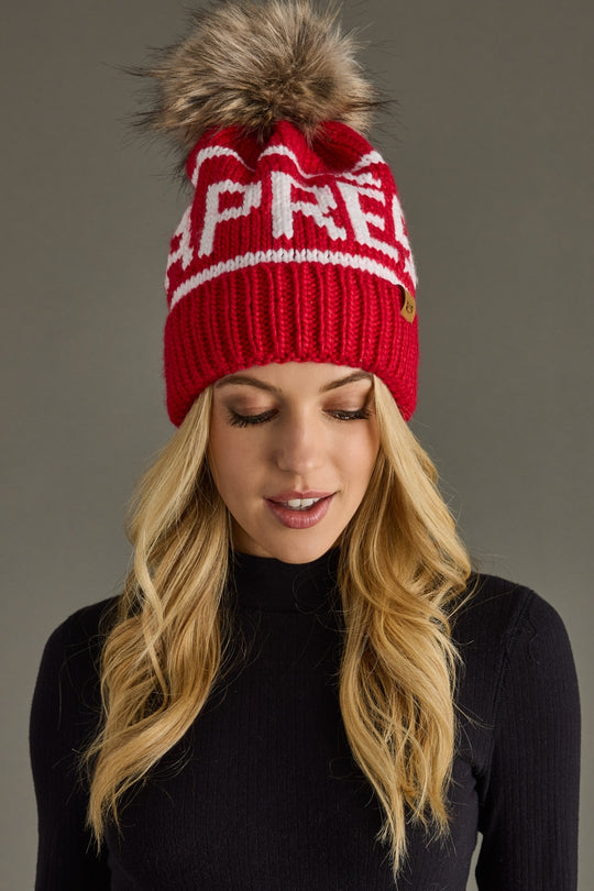 Woman wearing a red beanie with a fur pom-pom on a gray background