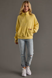 Woman wearing a yellow hoodie and light blue jeans on a gray background