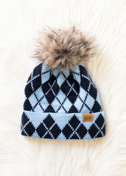 Blue and navy argyle patterned beanie with a fur pom-pom on a white fur surface