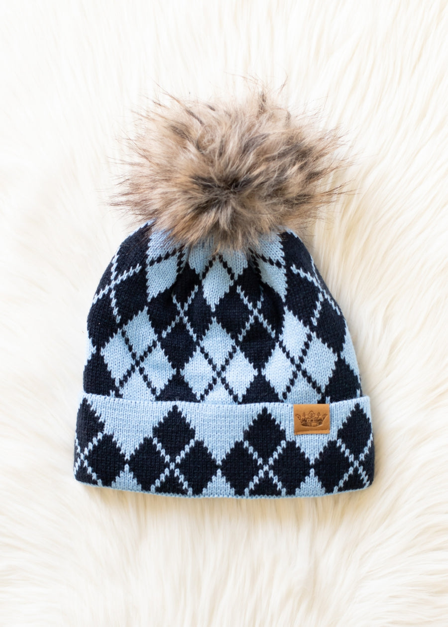 Blue and navy argyle patterned beanie with a fur pom-pom on a white fur surface