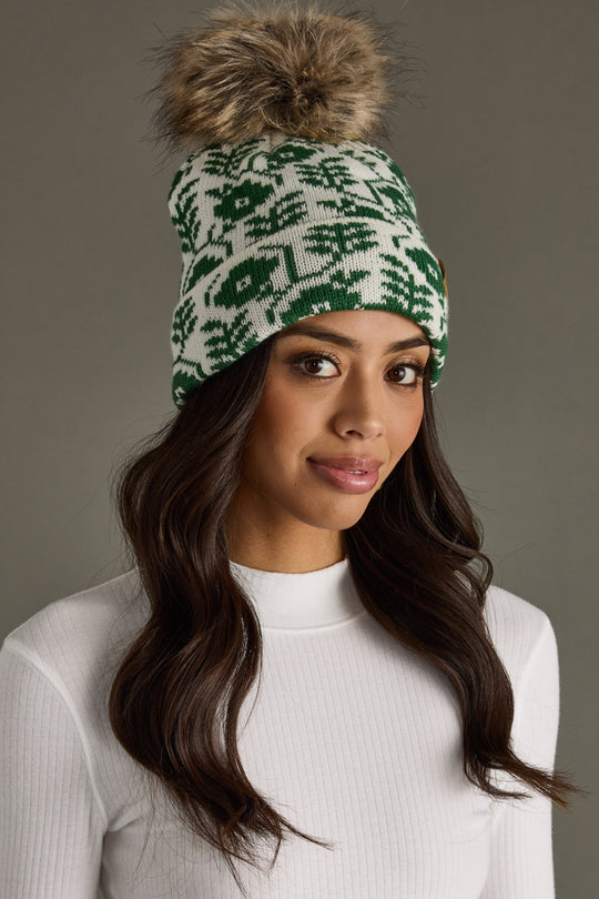 Woman wearing a green and white patterned beanie with a fur pom-pom on a gray background