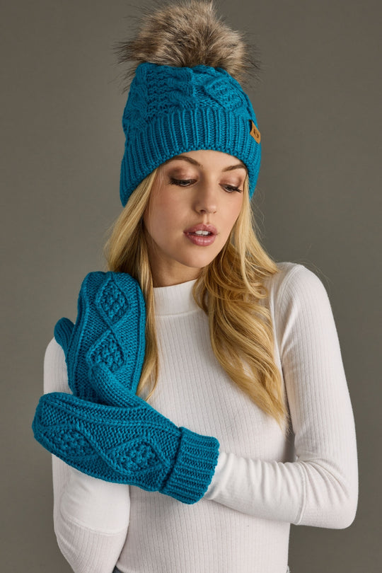 Woman wearing a blue knit beanie and gloves with a gray background