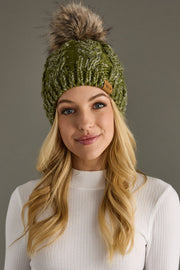 Woman wearing a green knitted beanie with a fur pom-pom against a gray background