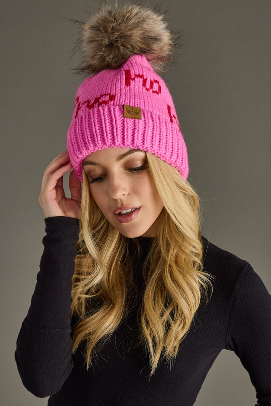 Woman wearing a pink beanie with a fur pom-pom on a gray background