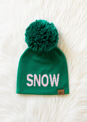 Green beanie with pom-pom and 'SNOW' text on a white fluffy background