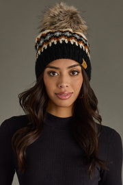 Woman wearing a black knit beanie with a fur pom-pom against a gray background