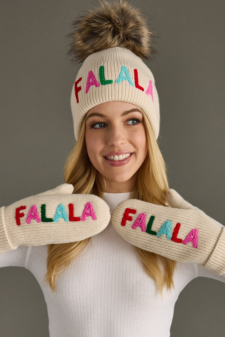 Person wearing a cream beanie and mittens with 'FALALA' text on a gray background