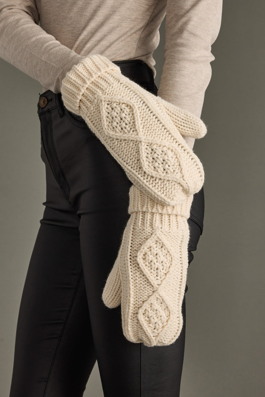Person wearing cream knitted mittens with a pattern against a neutral background