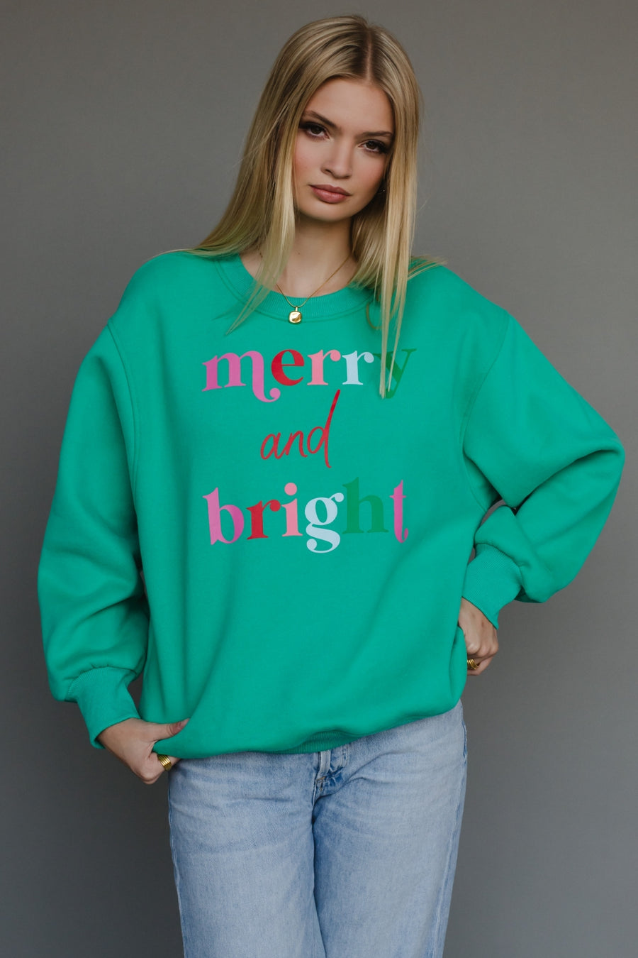 Woman wearing a green sweatshirt with 'merry and bright' text on a gray background