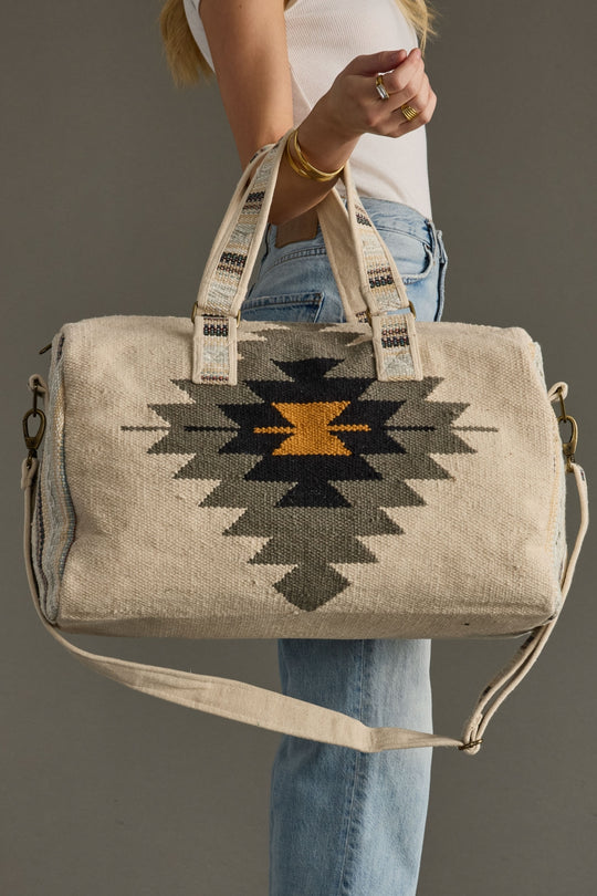 Person holding a beige tote bag with geometric pattern against a gray background