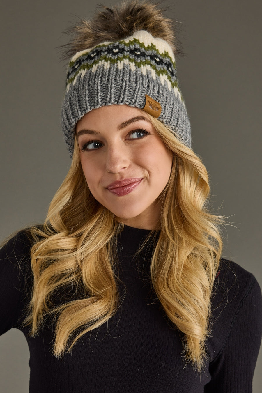 Woman wearing a striped knit beanie with a pom-pom on a gray background