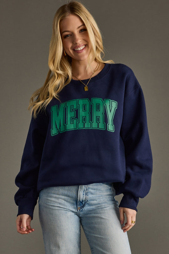 Woman wearing a navy sweatshirt with 'MERRY' in green text on a gray background