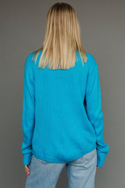 Person wearing a blue sweater and jeans against a gray background