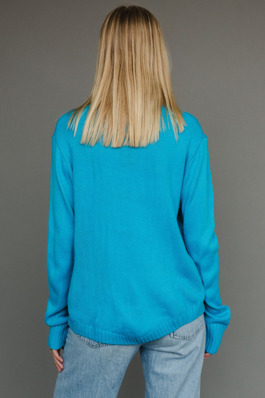 Person wearing a blue sweater and jeans against a gray background