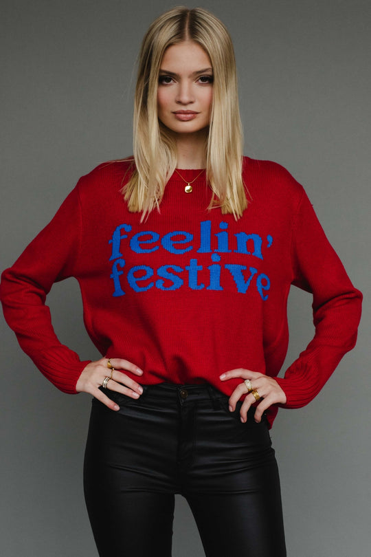 Person wearing a red sweater with 'feelin' festive' text on a gray background