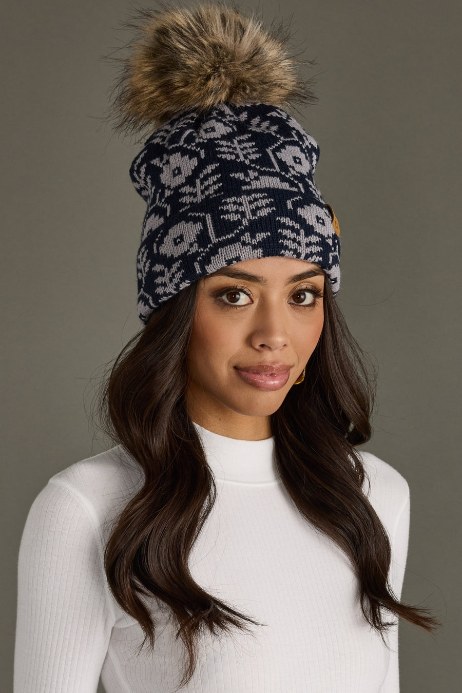 Woman wearing a patterned beanie with a pom-pom on a gray background