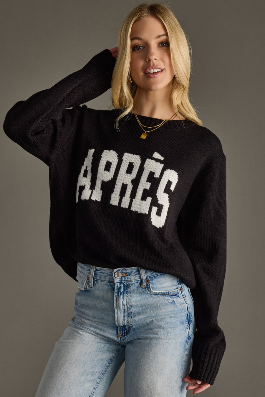 Woman wearing a black sweater with 'APRèS' text and blue jeans on a gray background
