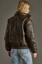 Person wearing a brown leather jacket and blue jeans against a gray background