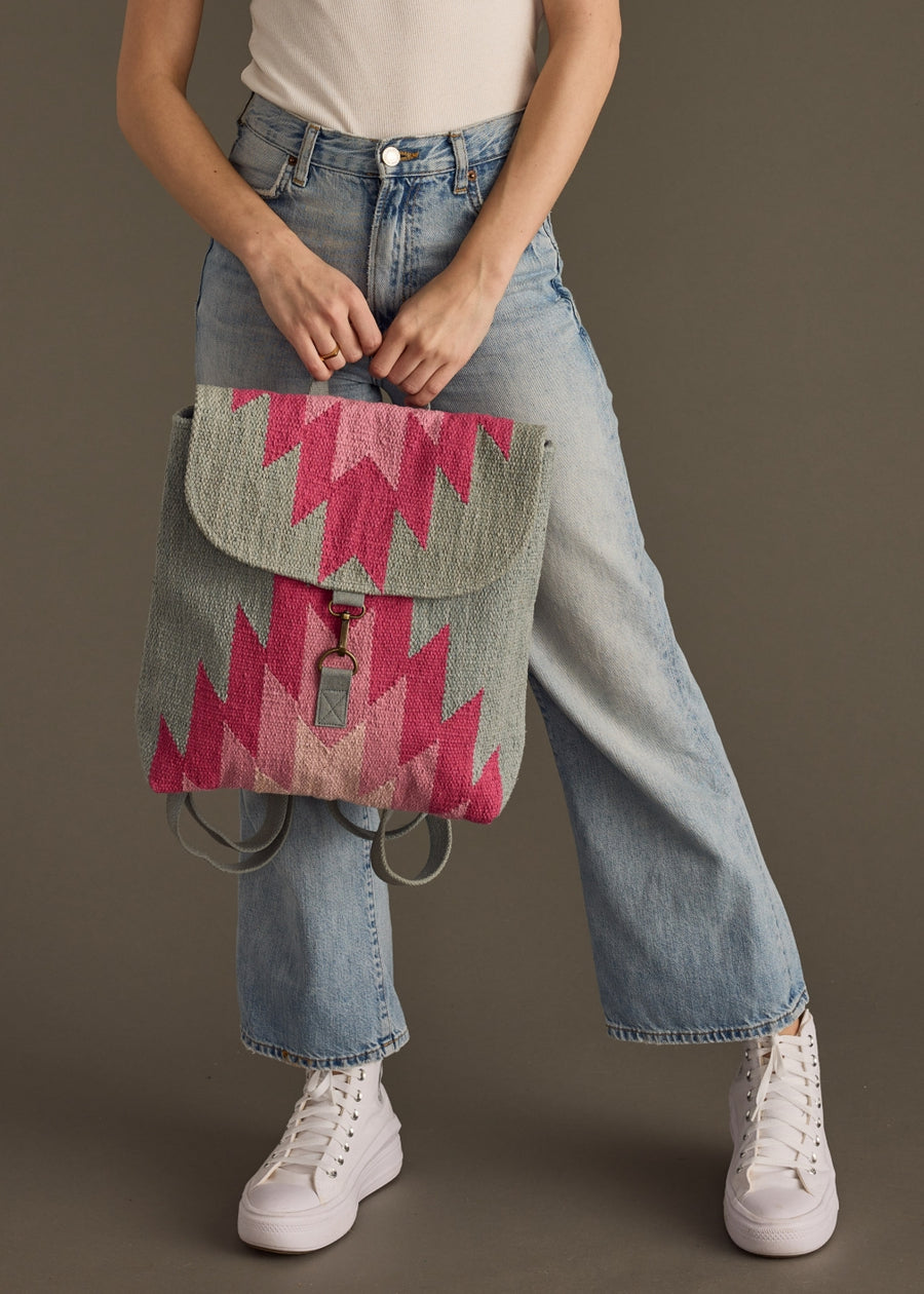 Person wearing a colorful backpack with a geometric pattern, standing against a plain background.