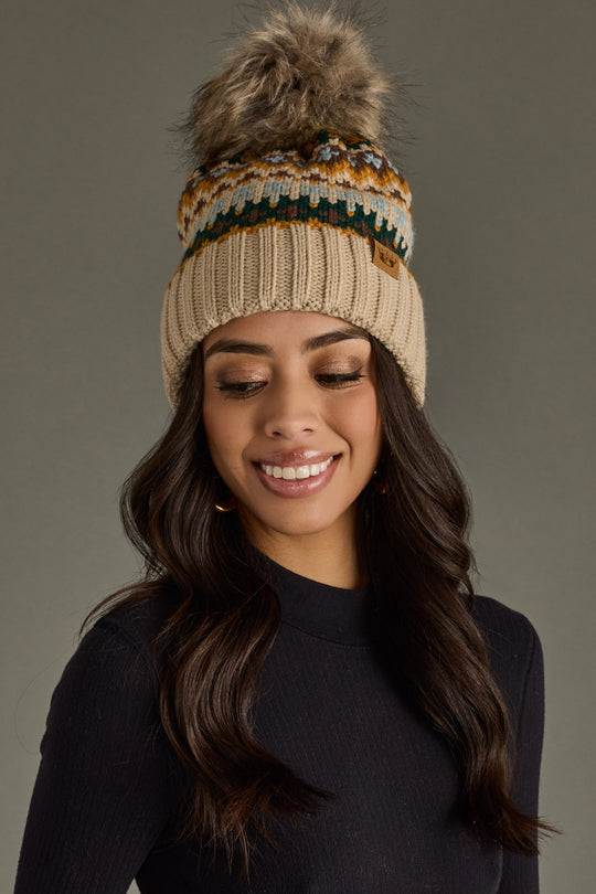Woman wearing a knitted beanie with a pom-pom against a gray background