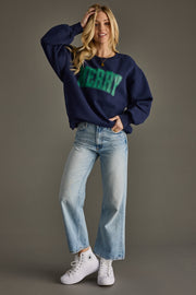 Woman wearing a navy sweatshirt with green text, light blue jeans, and white sneakers on a gray background