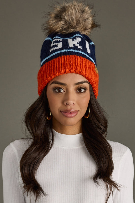 Woman wearing a colorful knit beanie with a pom-pom on a gray background