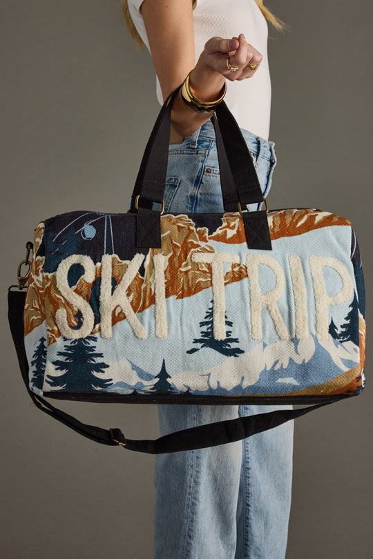 Person holding a duffel bag with 'Ski Trip' text and mountain design.