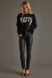 Woman wearing a black sweater with 'merry' text and black pants on a gray background