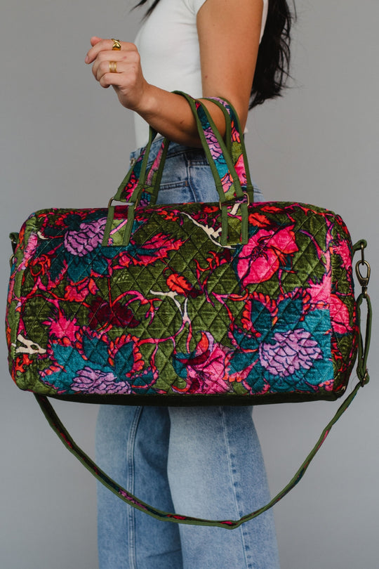 Person holding a colorful floral-patterned handbag against a gray background