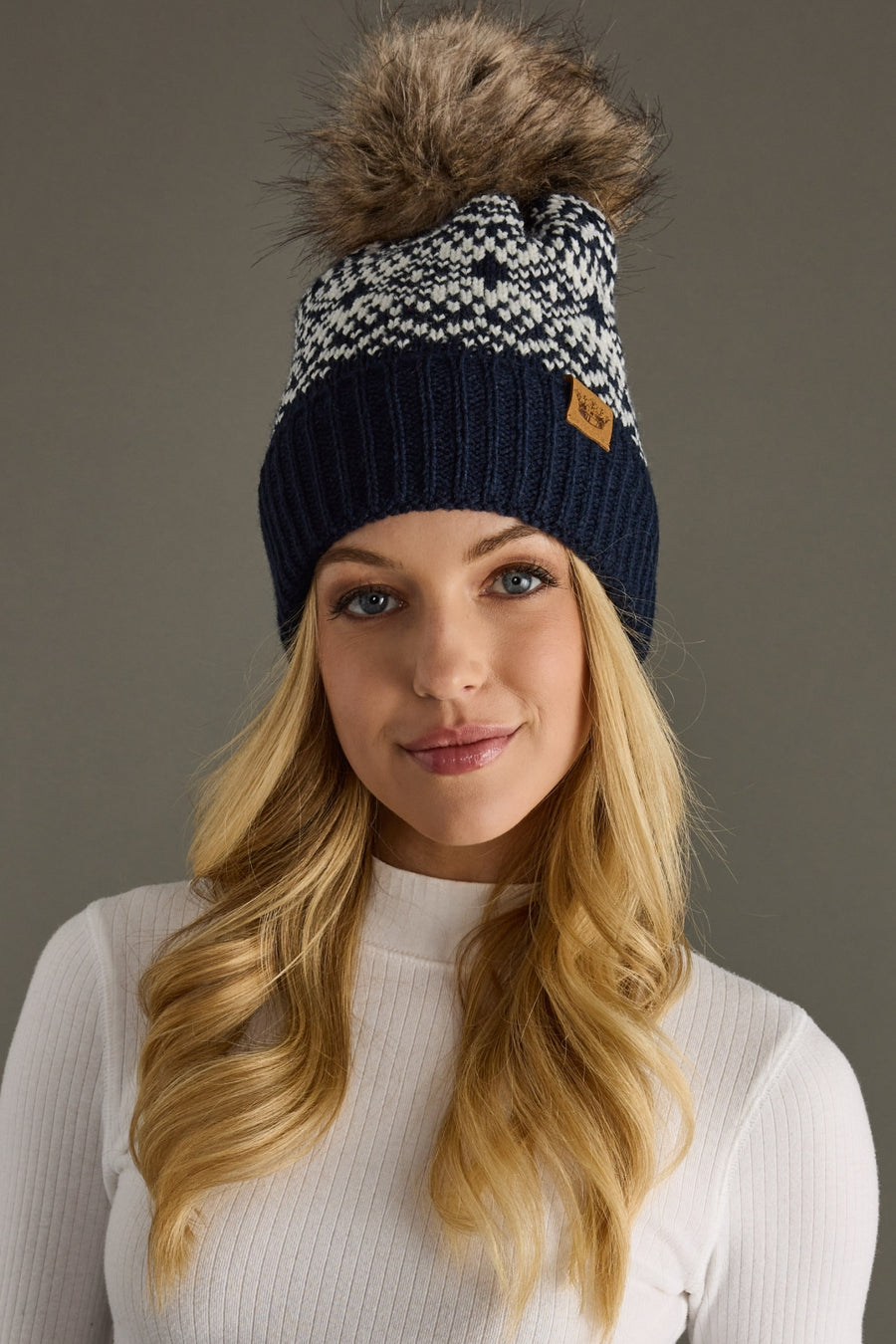 Woman wearing a dark navy and white patterned beanie with a pom-pom on a brown background