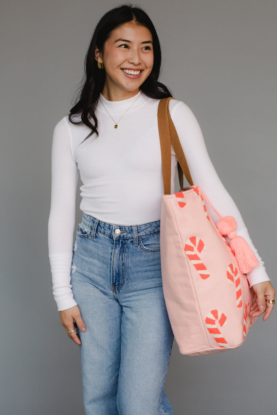 Woman holding a pink tote bag with candy cane patterns against a gray background