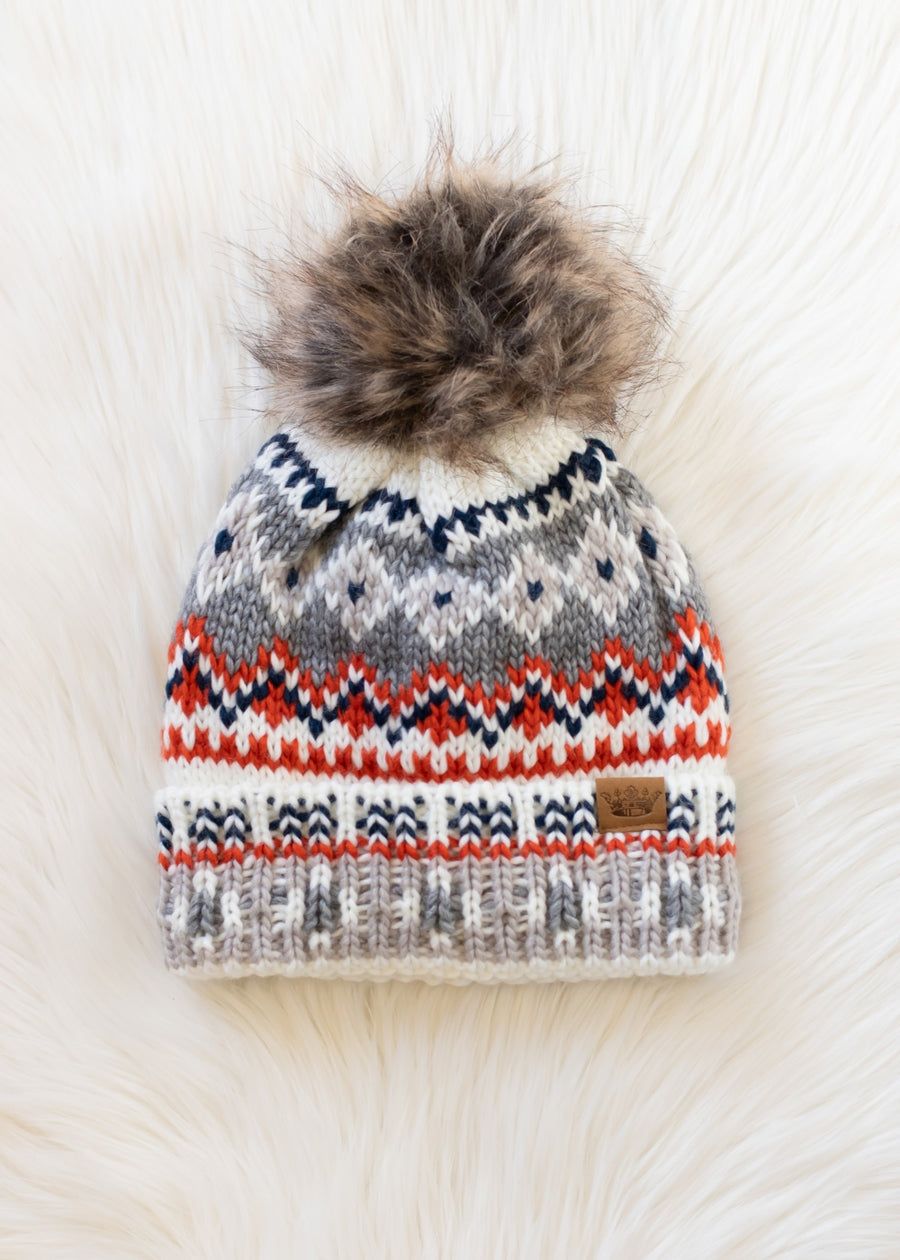 Knitted hat with a pattern and fur pom-pom on a white background