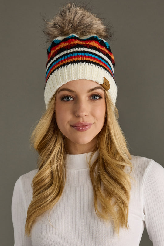 Woman wearing a colorful striped knit beanie against a gray background