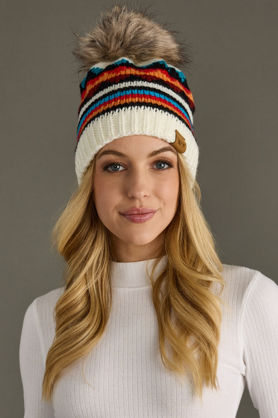 Woman wearing a colorful striped knit beanie against a gray background
