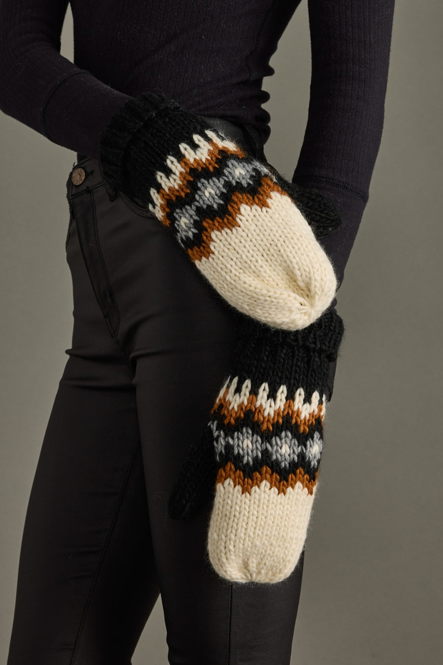 Knit mittens with a striped pattern worn by a person against a gray background