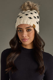 Woman wearing a patterned beanie with a fur pom-pom on a gray background