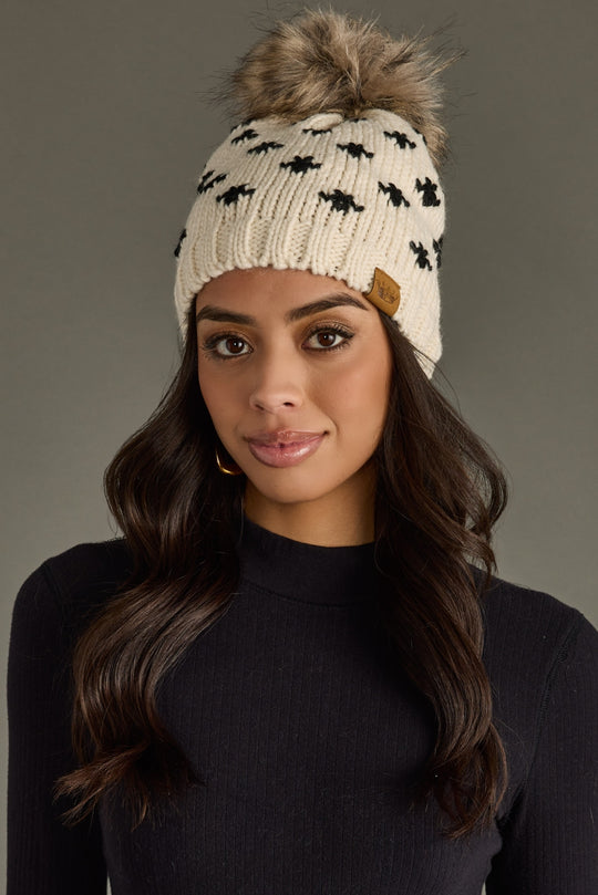 Woman wearing a patterned beanie with a fur pom-pom on a gray background