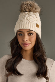 Woman wearing a cream knit beanie with a fur pom-pom against a gray background