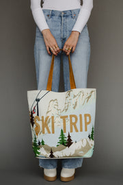Person holding a tote bag with ' ski trip' design against a gray background